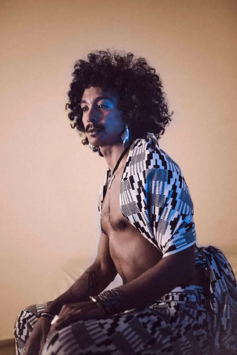 Portrait d'un homme aux cheveux afro bouclés, vêtu d'un ensemble wax noir et blanc, éclairé par un contraste dramatique de lumière bleue froide et chaude ambrée