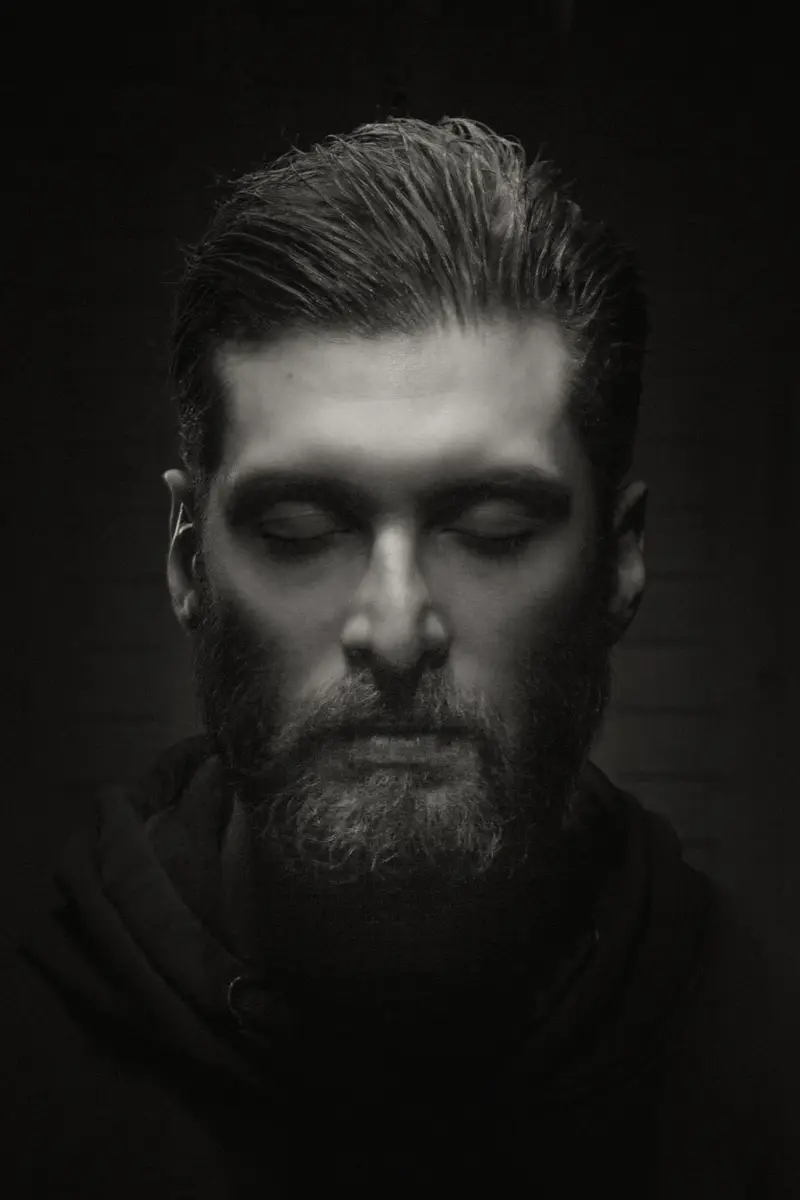 Portrait d'un homme barbu aux yeux fermés, baigné d'un éclairage dramatique de haut en style clair-obscur classique