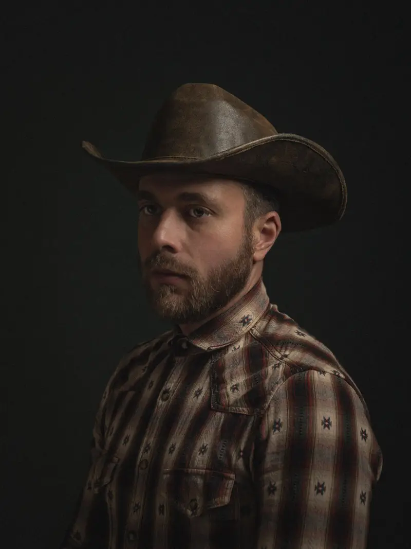 Portrait d'un cowboy en chapeau de cuir et chemise western, éclairé par un clair-obscur dramatique sur fond noir dans un style néo-classique flamand