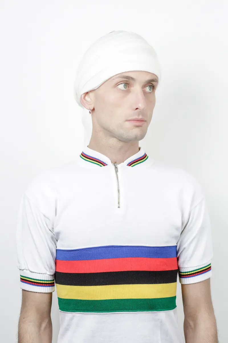 Portrait en studio d'un cycliste en maillot blanc à bandes arc-en-ciel, éclairage doux et uniforme sur fond blanc, style minimaliste et clinique