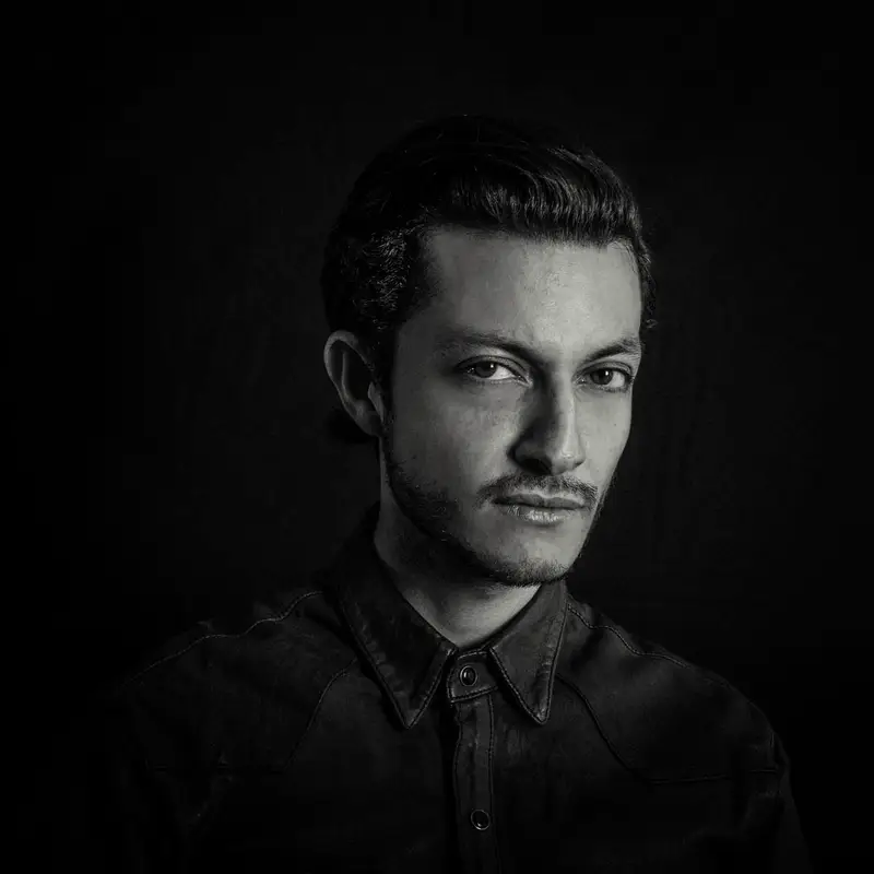 Portrait d'un jeune homme au regard intense, éclairé par un clair-obscur dramatique sur fond noir, dans un style photographique monochrome et cinématographique