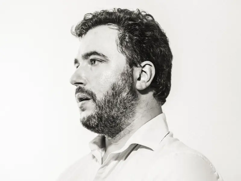 Portrait en noir et blanc d'un homme barbu de profil, éclairé par une lumière forte et contrastée sur fond blanc immaculé, dans un style minimaliste et élégant