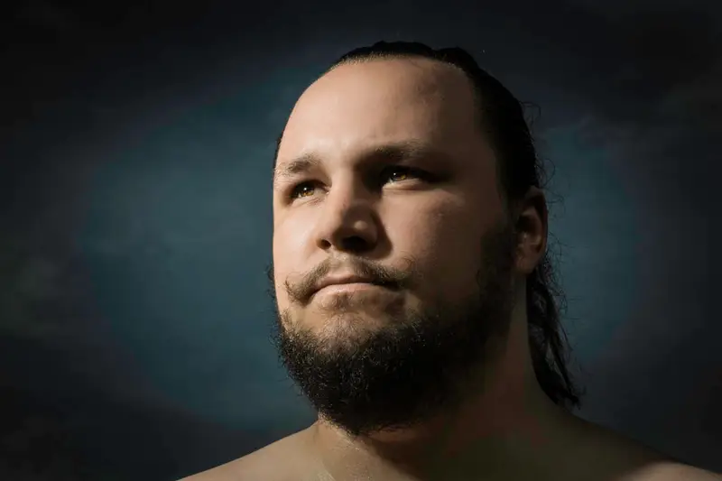 Portrait d'un homme barbu aux cheveux longs, éclairé par un chiaroscuro dramatique dans un style classique et cinématographique
