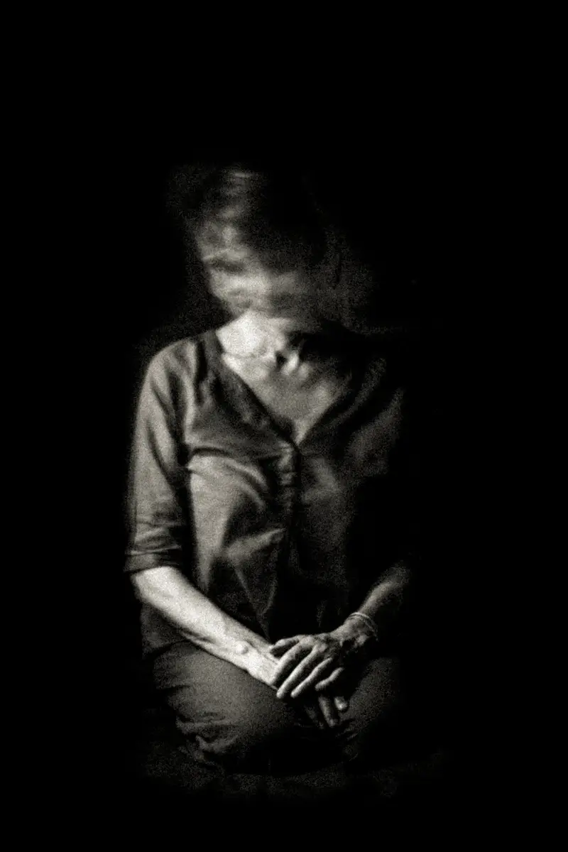 Femme assise de face, mains jointes, visage flouté par effet de mouvement vertical, fond noir