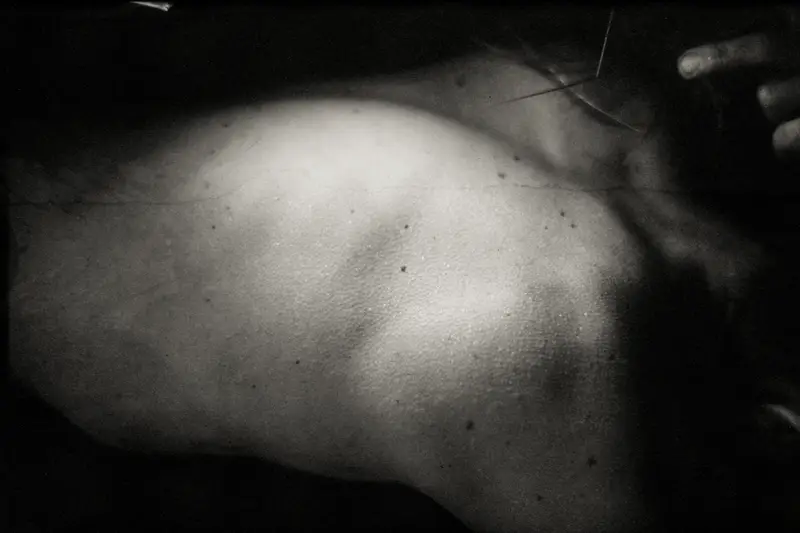 Homme torse nu tenant un crâne animal devant son visage, texture granuleuse, fond noir