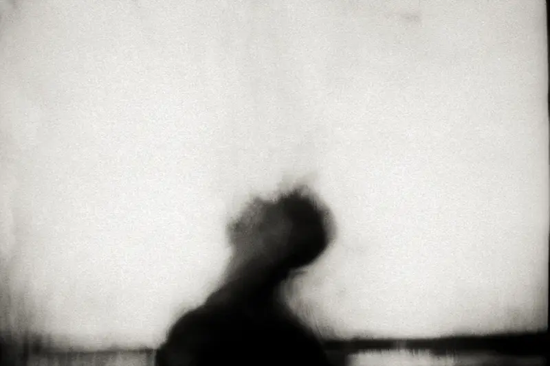 Silhouette floue et sombre d'une personne vue de dos, placée dans le tiers inférieur d'un vaste fond blanc